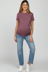 woman wearing a mauve short sleeve maternity top and distressed blue jeans, showing her baby bump