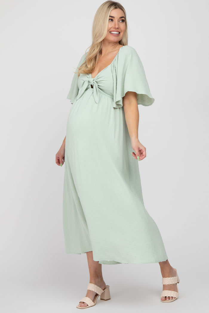 woman wearing a light green maternity dress with a tie front and flutter sleeves, showing her baby bump