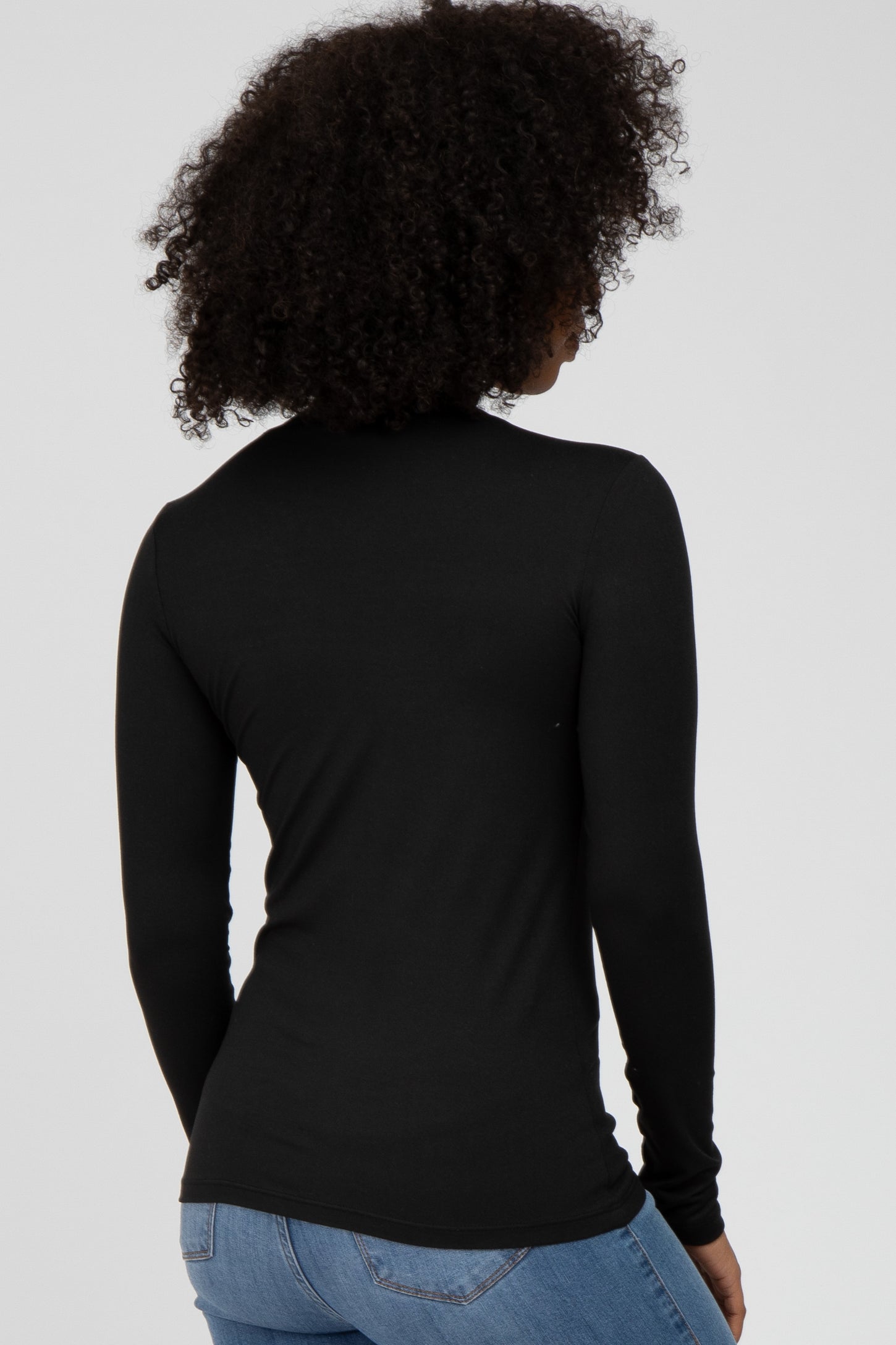 woman wearing a fitted black long sleeve top, viewed from the back, paired with light blue jeans