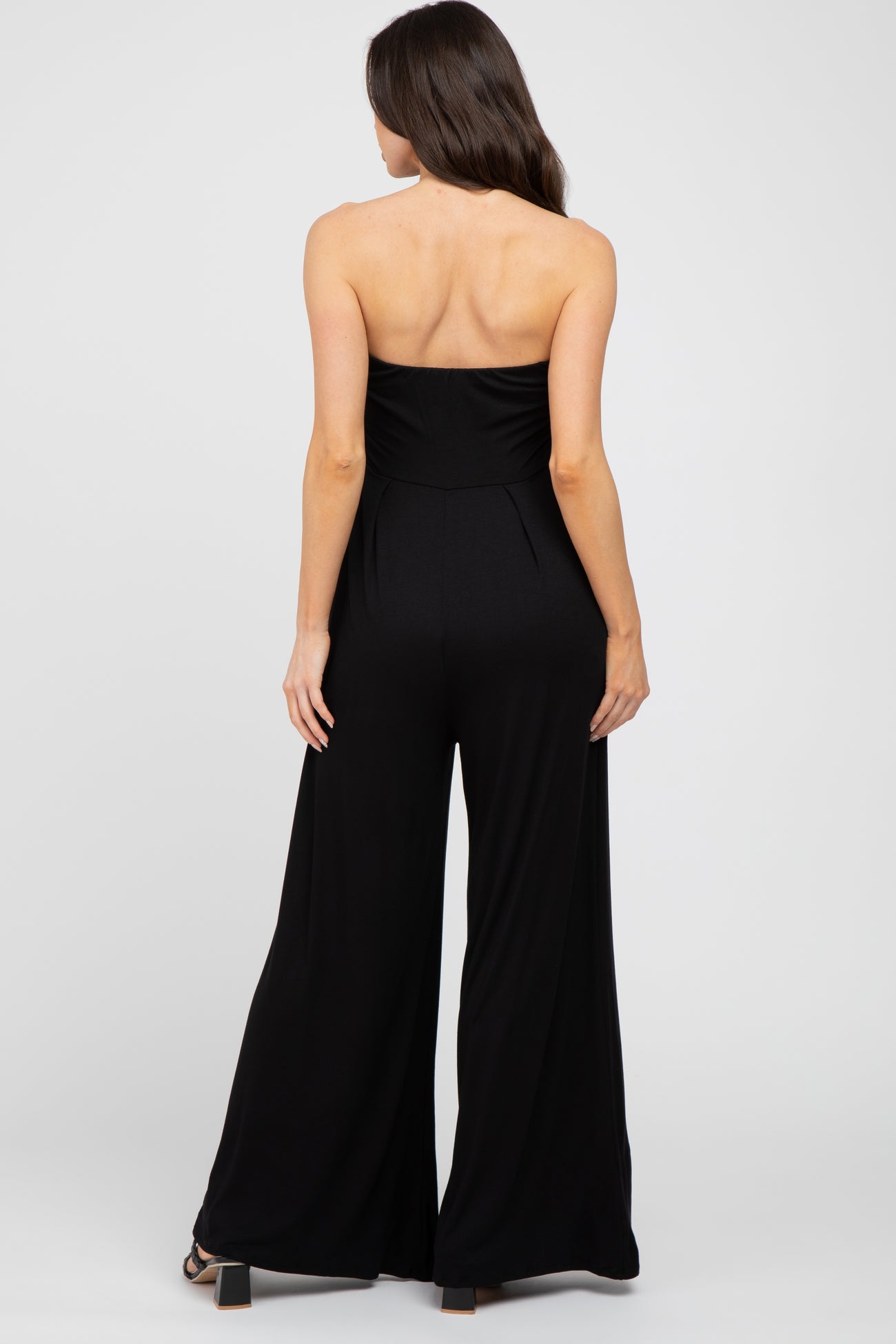 woman wearing a black strapless maternity jumpsuit, back view, with wide legs and a fitted bodice