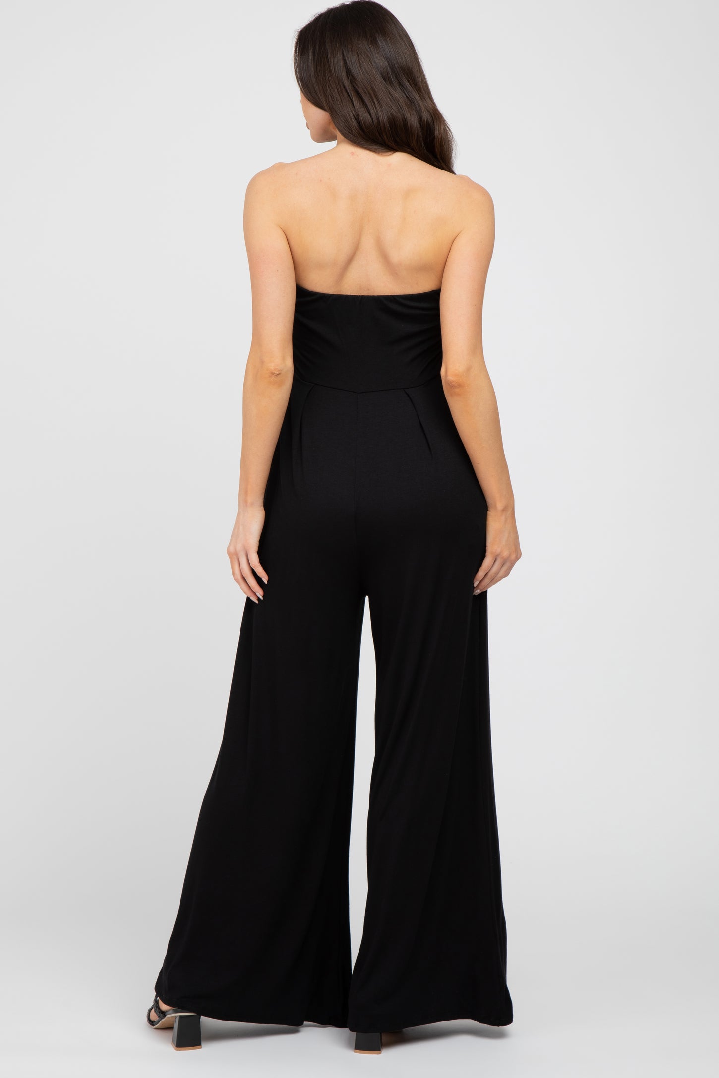 woman wearing a black strapless maternity jumpsuit, back view, with wide legs and a fitted bodice