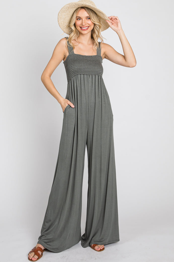 woman wearing olive green smocked wide leg jumpsuit and straw sun hat against white background