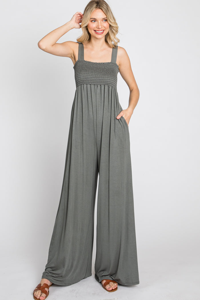 woman wearing olive green smocked wide leg jumpsuit with pockets and brown sandals