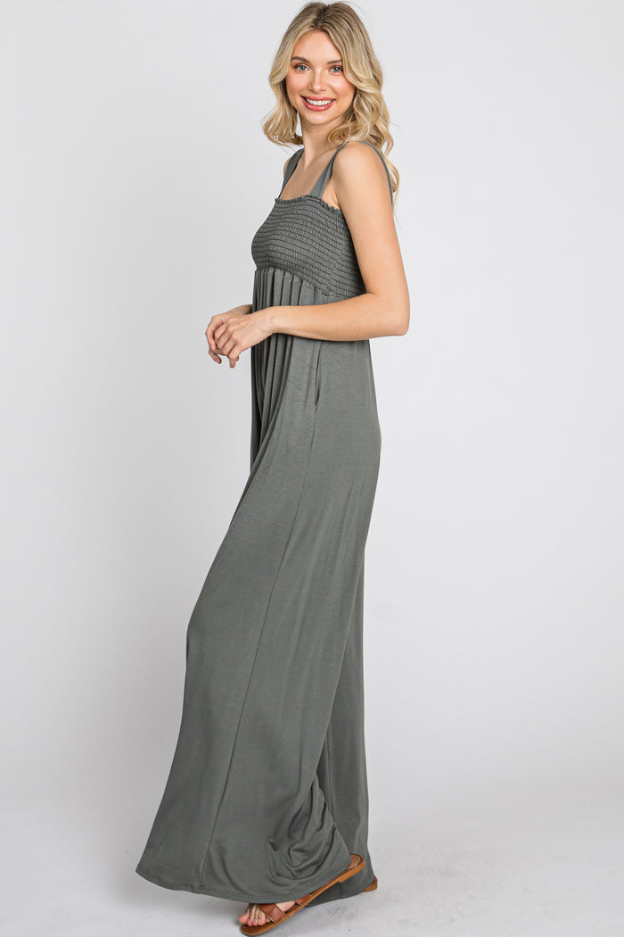 woman wearing a charcoal grey smocked wide leg jumpsuit with pockets and brown sandals