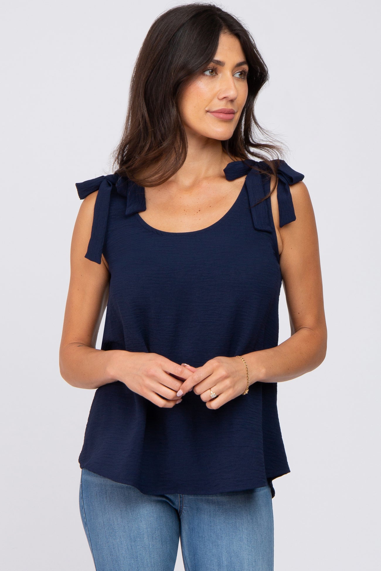 woman wearing a navy blue sleeveless top with tie details on the shoulders and paired with light blue jeans