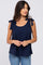 woman wearing a navy blue sleeveless top with tie details on the shoulders and paired with light blue jeans