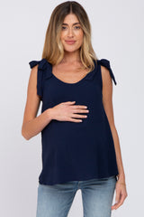 woman wearing a navy blue maternity top with tie shoulder details and holding her baby bump