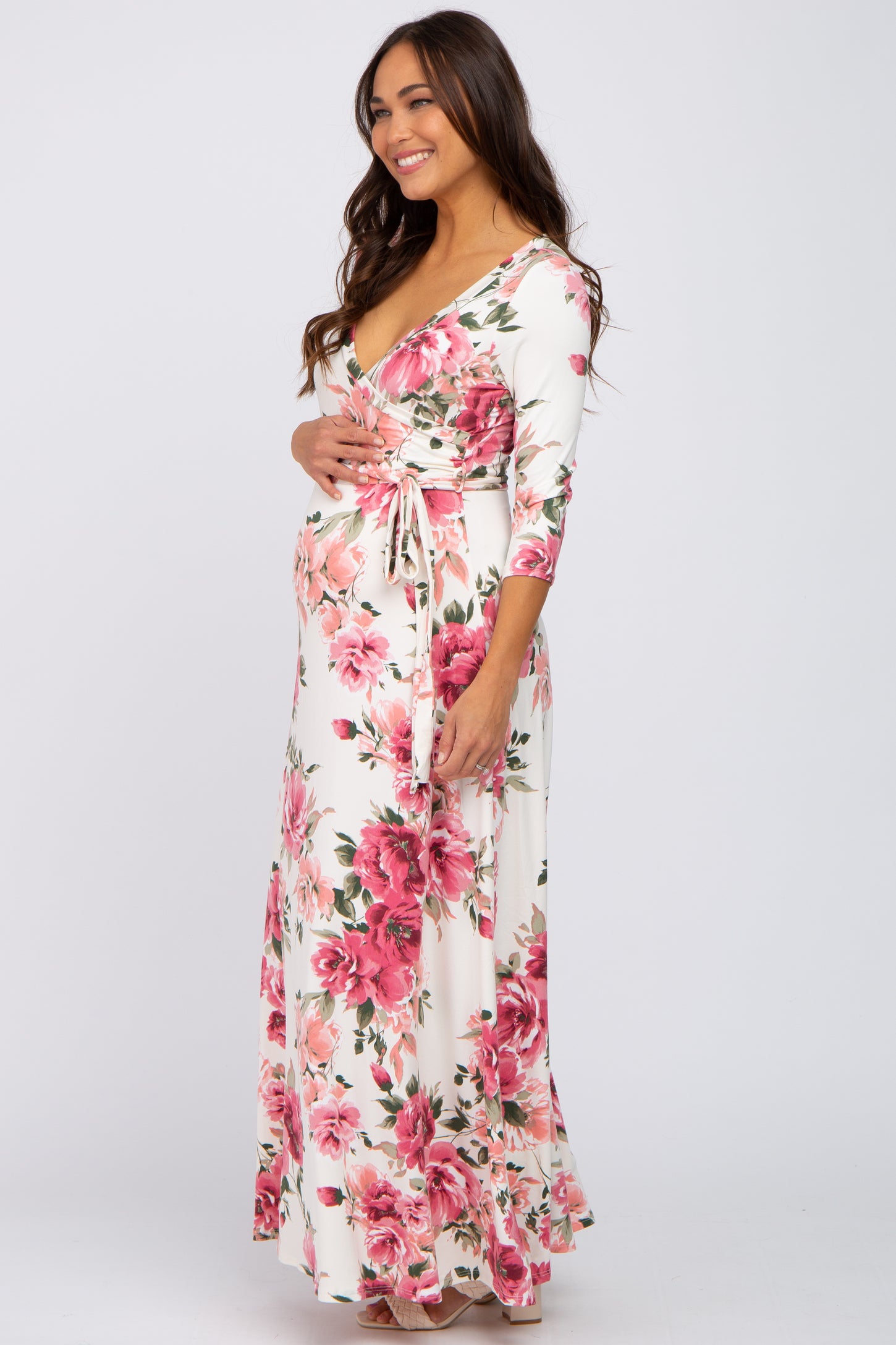 woman wearing a white floral print maternity maxi dress and holding her baby bump