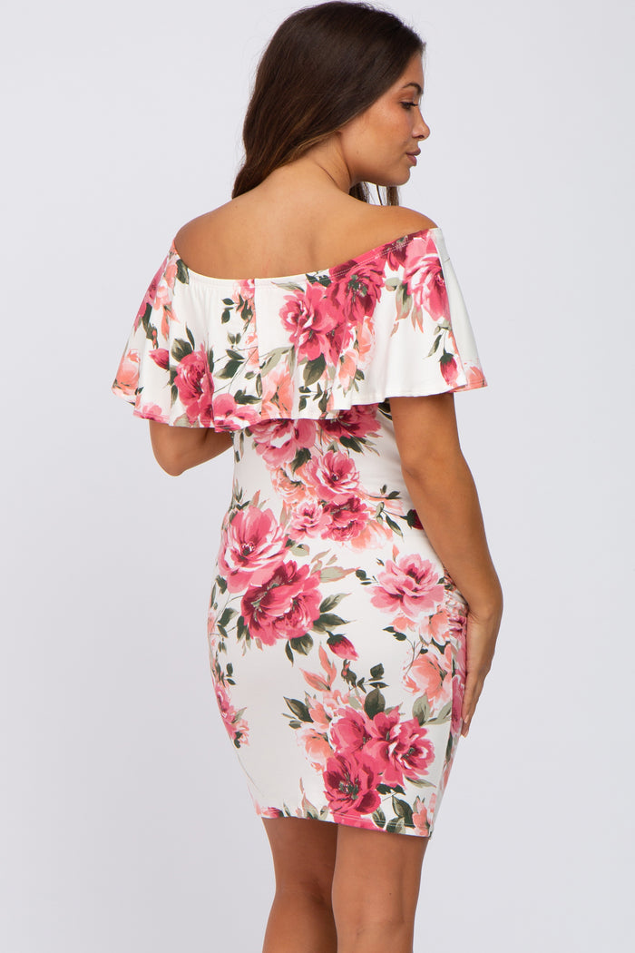 Woman wearing a white off-the-shoulder maternity dress with a pink floral print and ruffle neckline