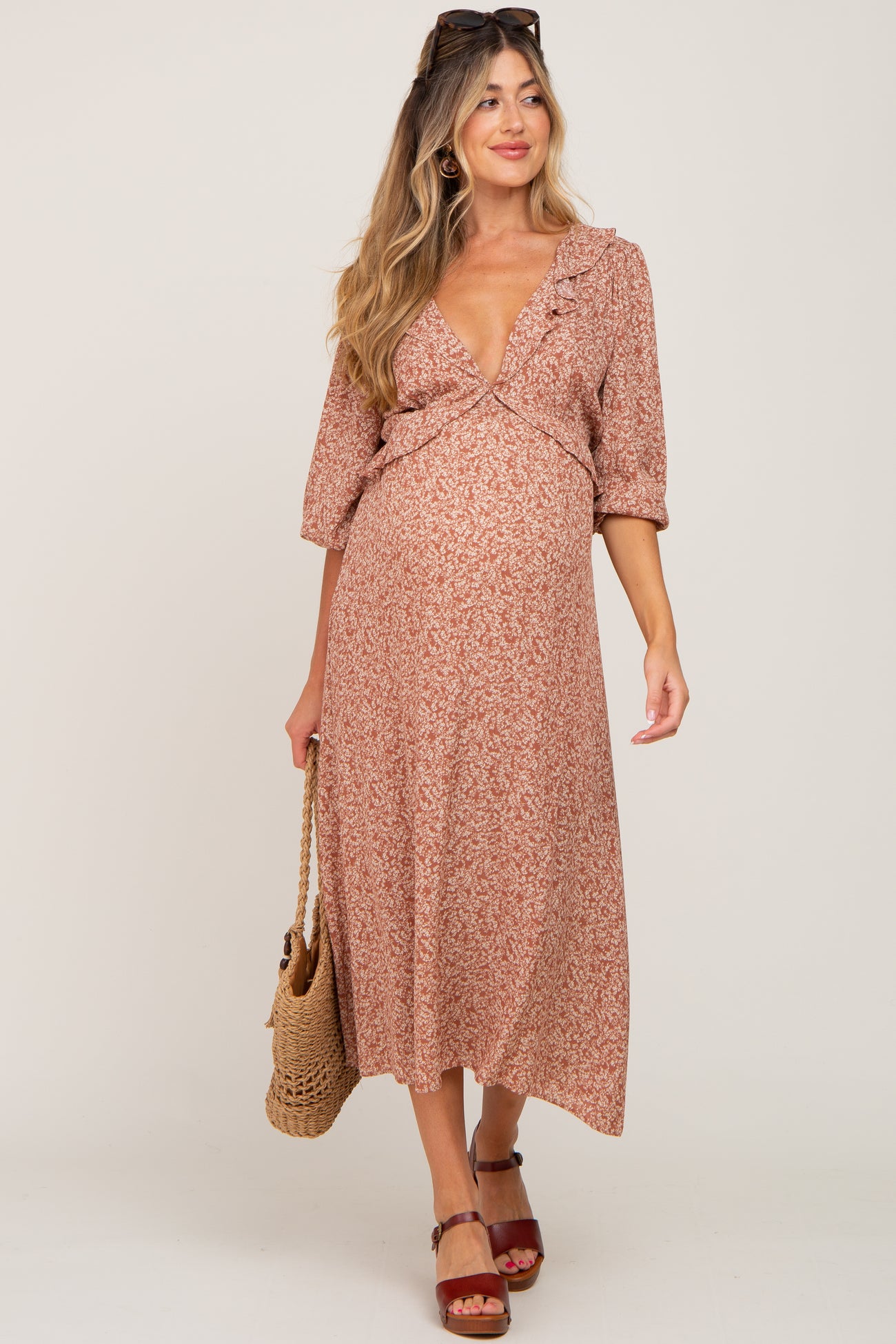 woman wearing a floral maternity dress with a deep v-neck and ruffle detailing, holding a woven bag and showing her baby bump