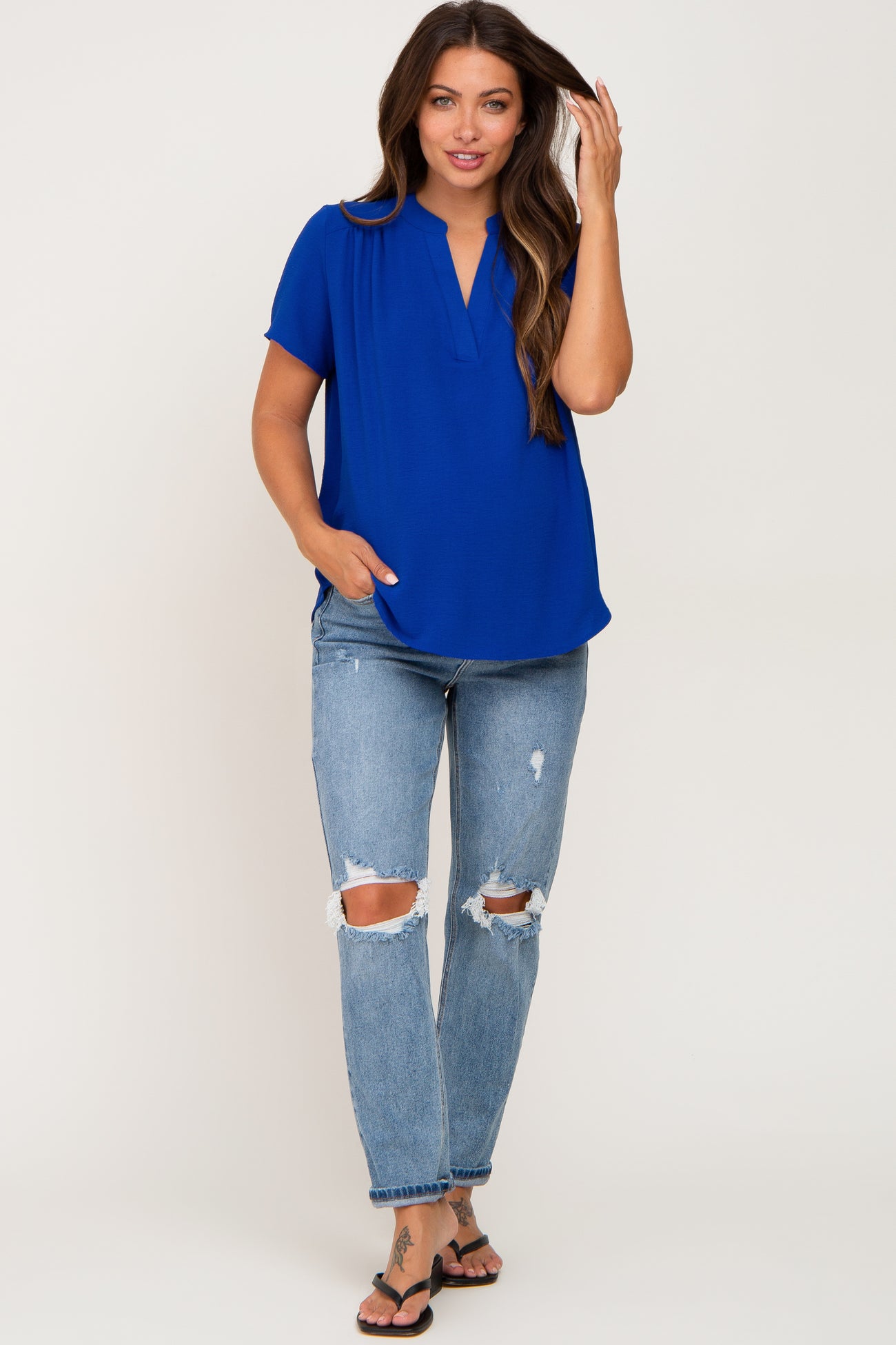 woman wearing a vibrant blue short sleeve maternity top with a v-neck and distressed light wash jeans