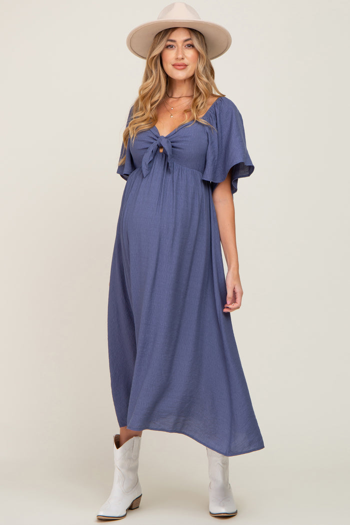 woman wearing a blue maternity dress with a front tie detail and flutter sleeves, showcasing her baby bump