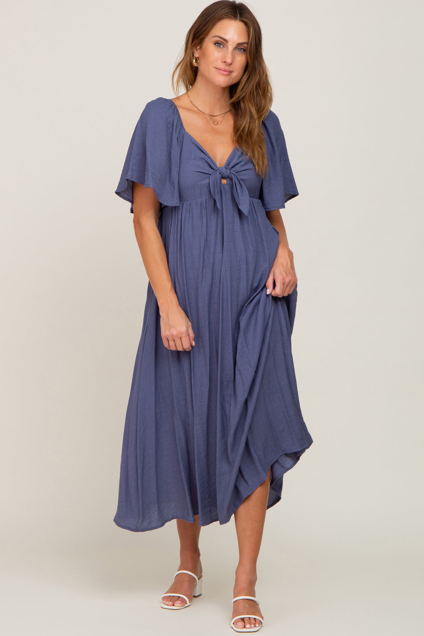 woman wearing a navy blue maxi dress with a tie front and flutter sleeves, standing and smiling