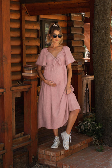 woman wearing a dusty pink maternity dress with a v-neck and short sleeves, holding her baby bump