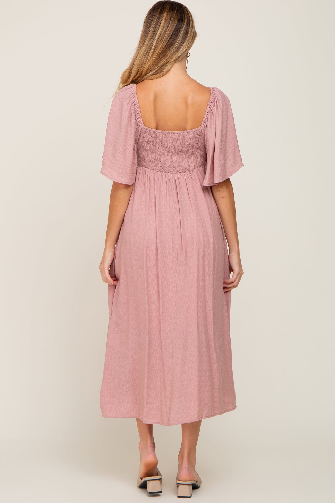 woman wearing a pink maternity dress with short sleeves and a smocked bodice, showing the back view