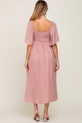 woman wearing a pink maternity dress with short sleeves and a smocked bodice, showing the back view