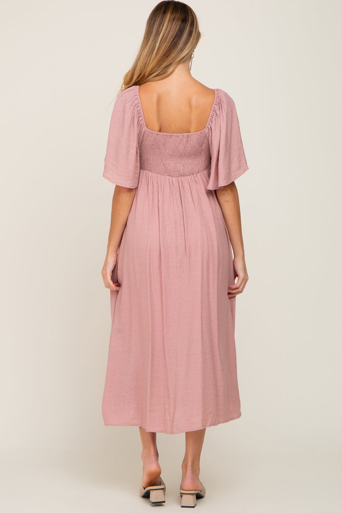 woman wearing a pink maternity dress with short sleeves and a smocked bodice, showing the back view