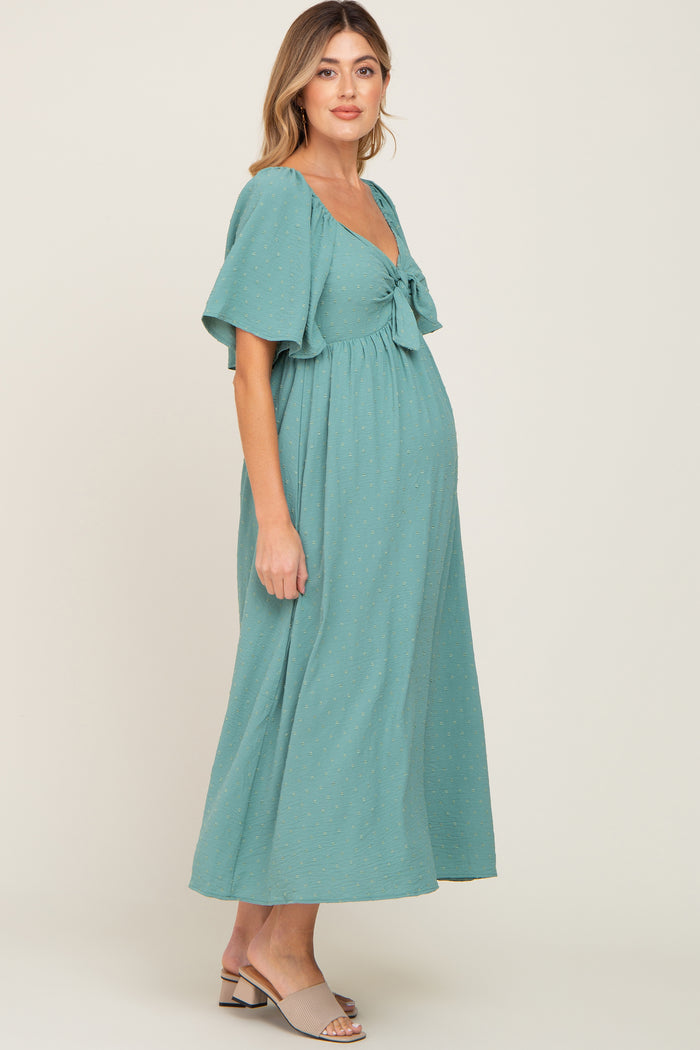 woman wearing a teal maternity dress with flutter sleeves and a tied waist, showcasing her baby bump