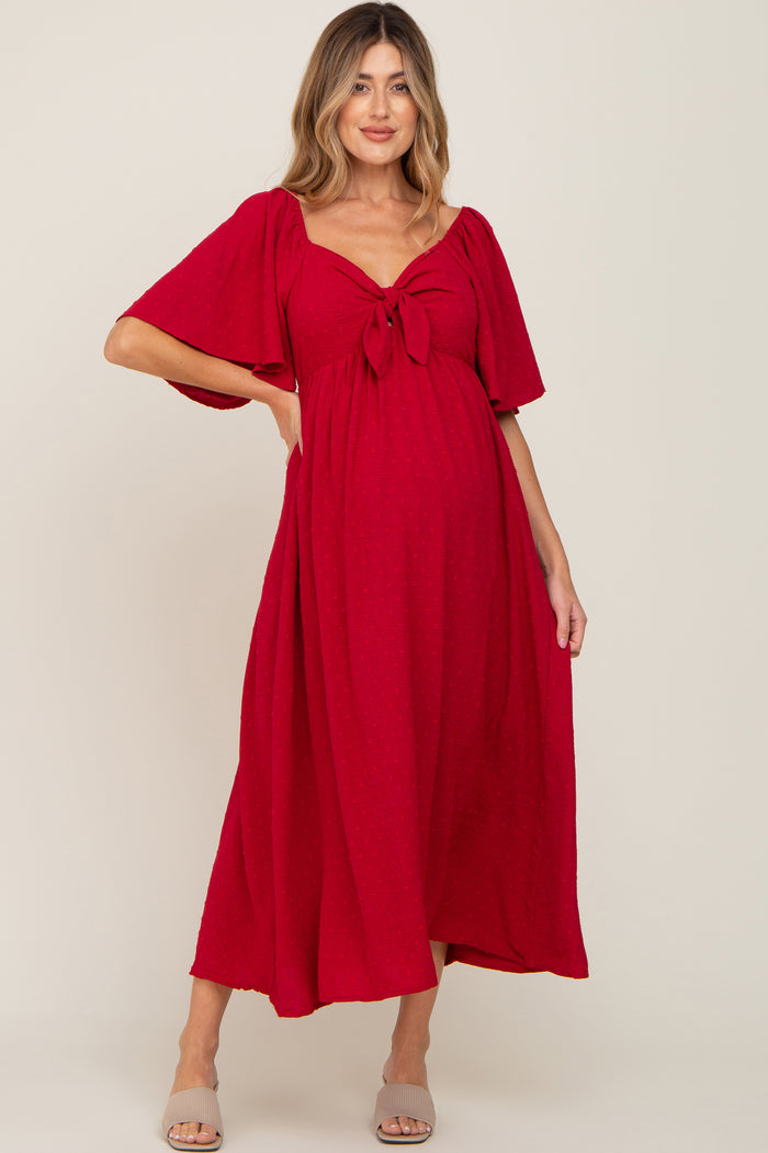 woman wearing a red maternity maxi dress with a tie front detail and short flutter sleeves, showcasing a visible baby bump