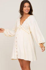 smiling pregnant woman wearing a cream maternity mini dress with lace bodice and long balloon sleeves