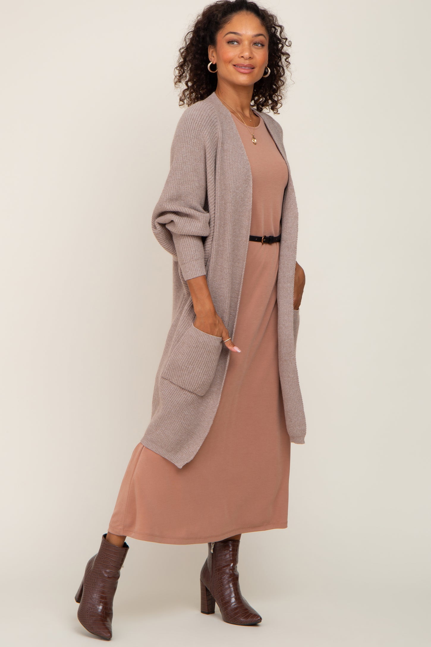 woman wearing a taupe long cardigan over a mauve maxi dress with a belt and brown ankle boots