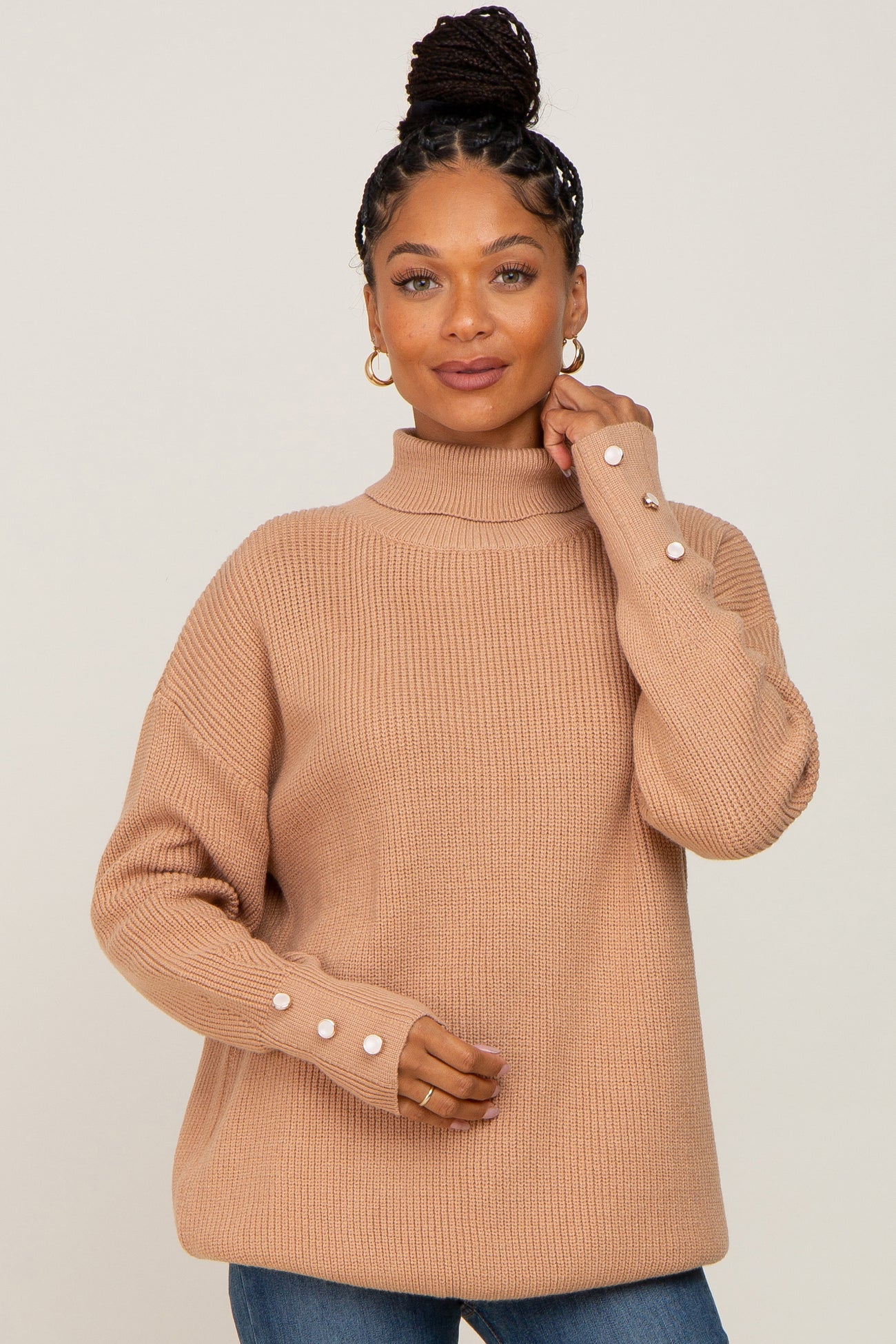 woman wearing a beige turtleneck sweater with ribbed texture and button details on the sleeves
