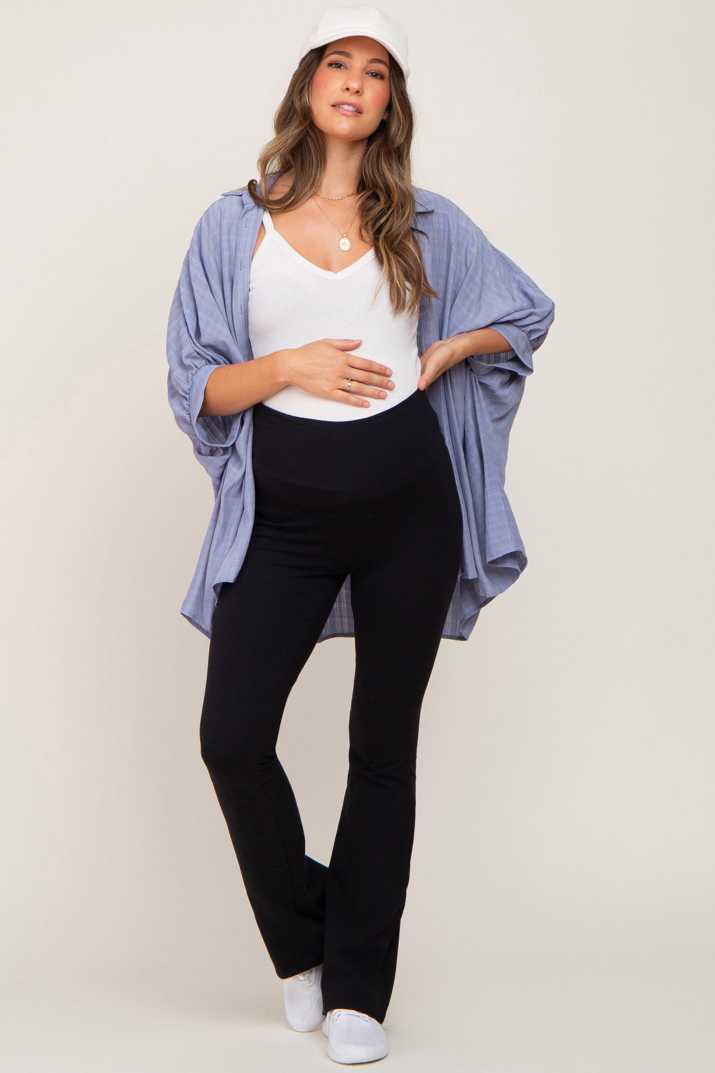 woman wearing a white maternity tank top, black maternity flared pants, and a blue button-up shirt, holding her baby bump