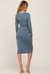 woman wearing a fitted dusty blue long sleeve maternity dress, showing a baby bump from the back