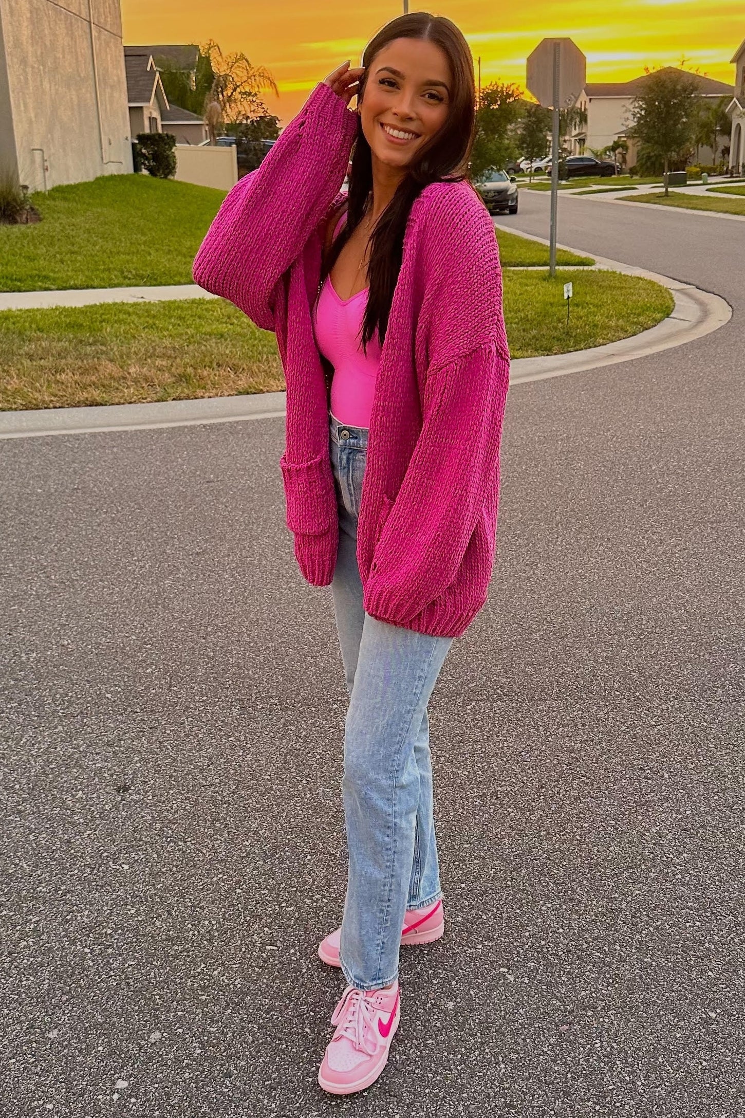 woman wearing a vibrant pink oversized cardigan, a pink bodysuit, and light wash flared jeans with pink sneakers