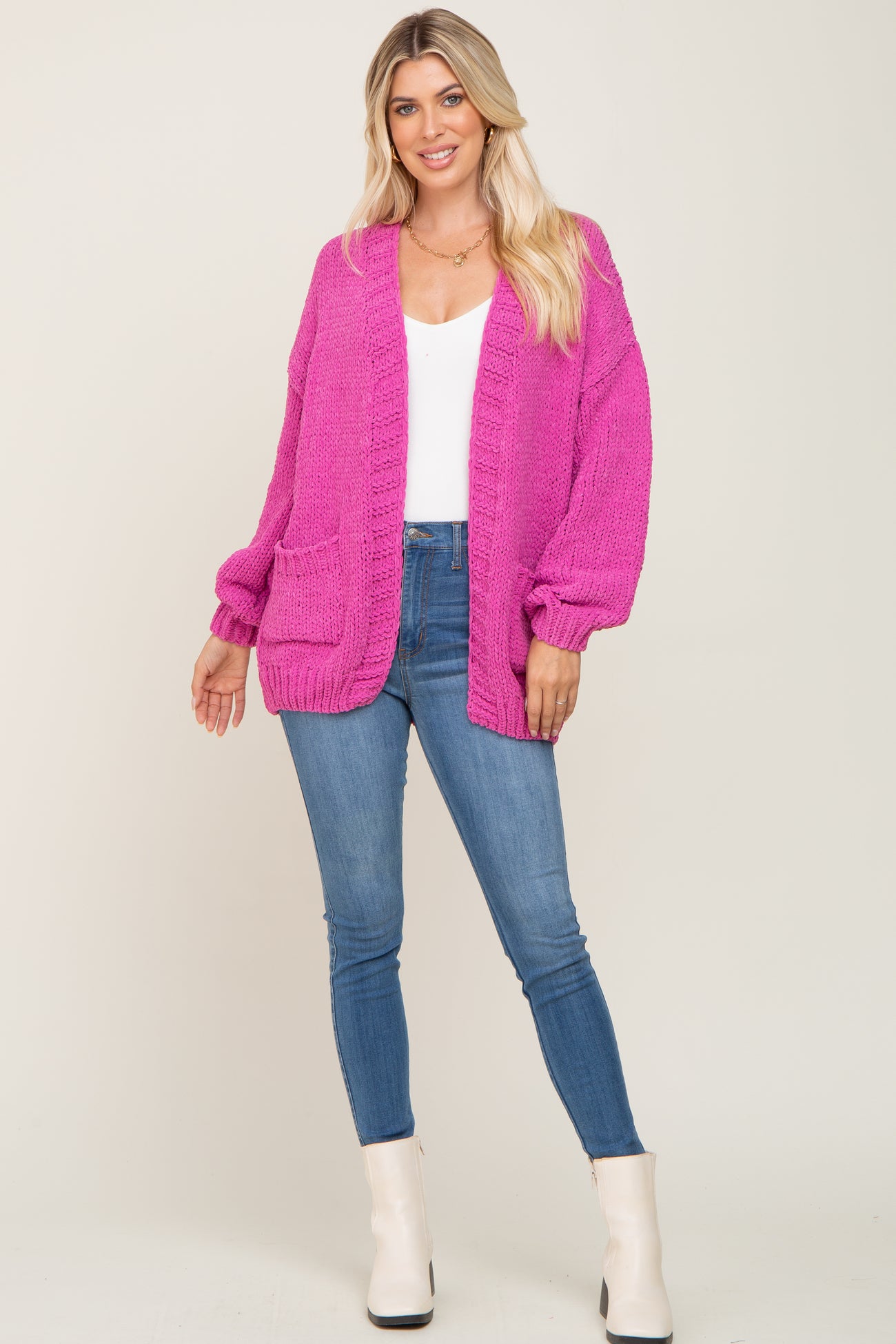 woman wearing a bright pink oversized knit cardigan with long sleeves and front pockets, paired with blue skinny jeans