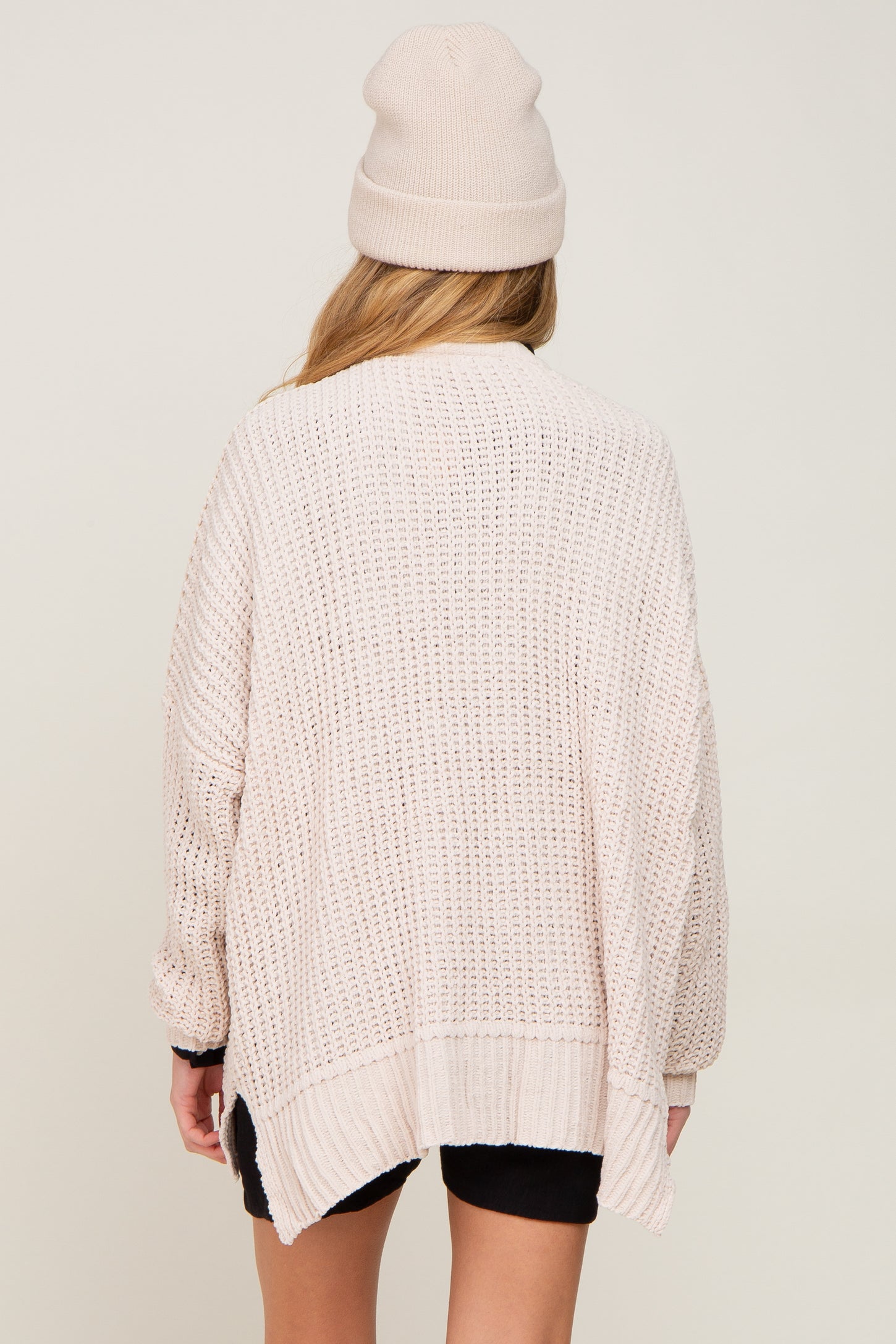 woman wearing a light pink oversized knit maternity cardigan and a matching beanie, viewed from the back
