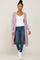 woman wearing a light purple long cardigan over a white top and blue jeans, walking in white ankle boots