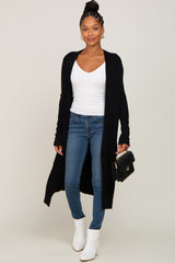 woman wearing a black long cardigan over a white v-neck top with skinny jeans and white ankle boots, holding a black clutch