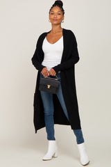 woman wearing long black cardigan white top blue jeans and white boots holding a black handbag