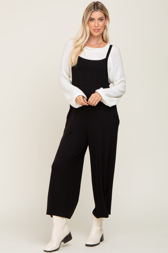 woman wearing a black jumpsuit over a white sweater and white ankle boots