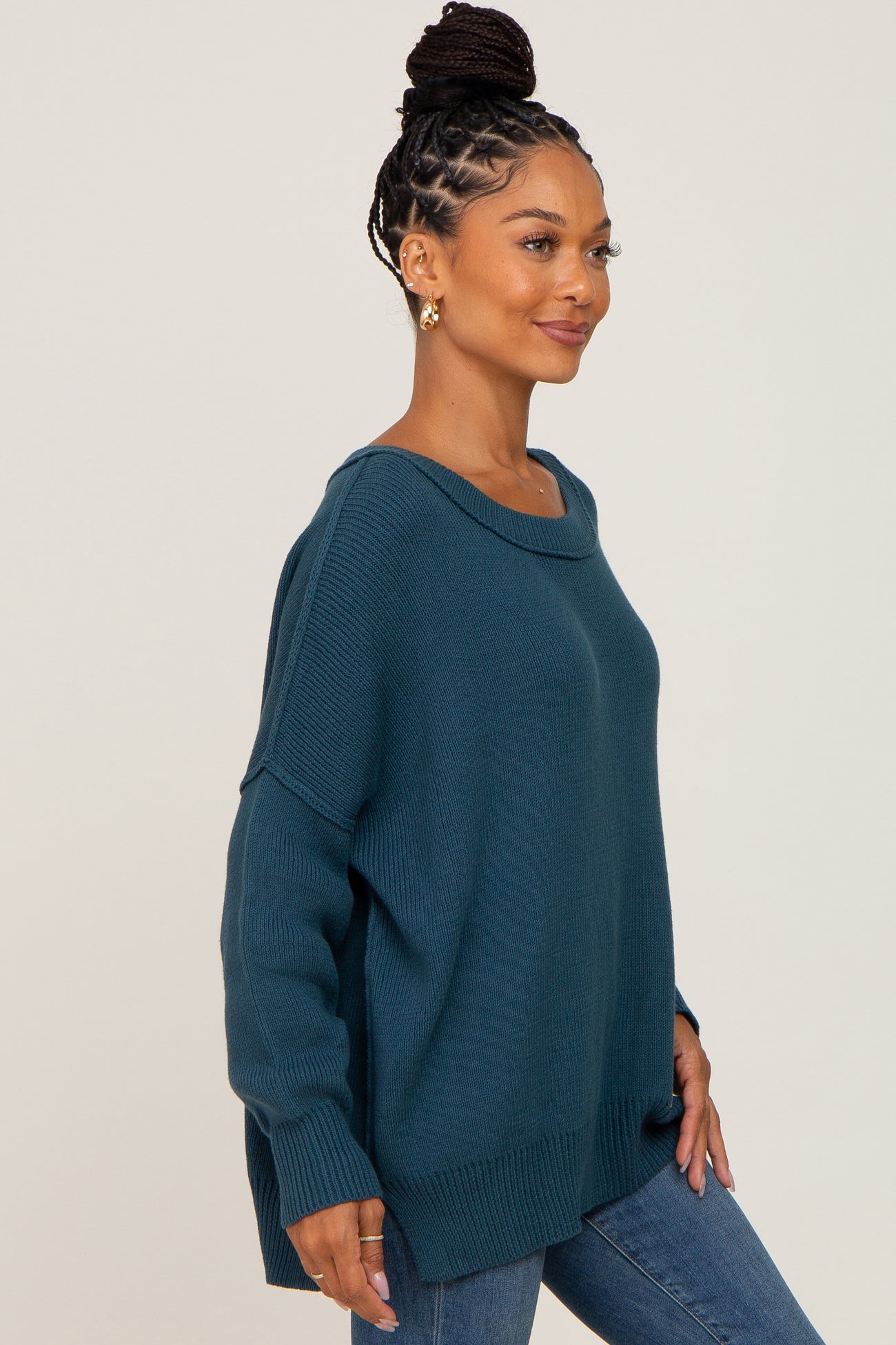woman wearing a teal oversized sweater with a scoop neck and long sleeves, paired with blue jeans