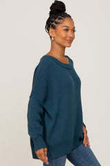 woman wearing a teal oversized sweater with a scoop neck and long sleeves, paired with blue jeans