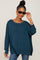 woman wearing a teal oversized knit sweater and stylish sunglasses, smiling at the camera