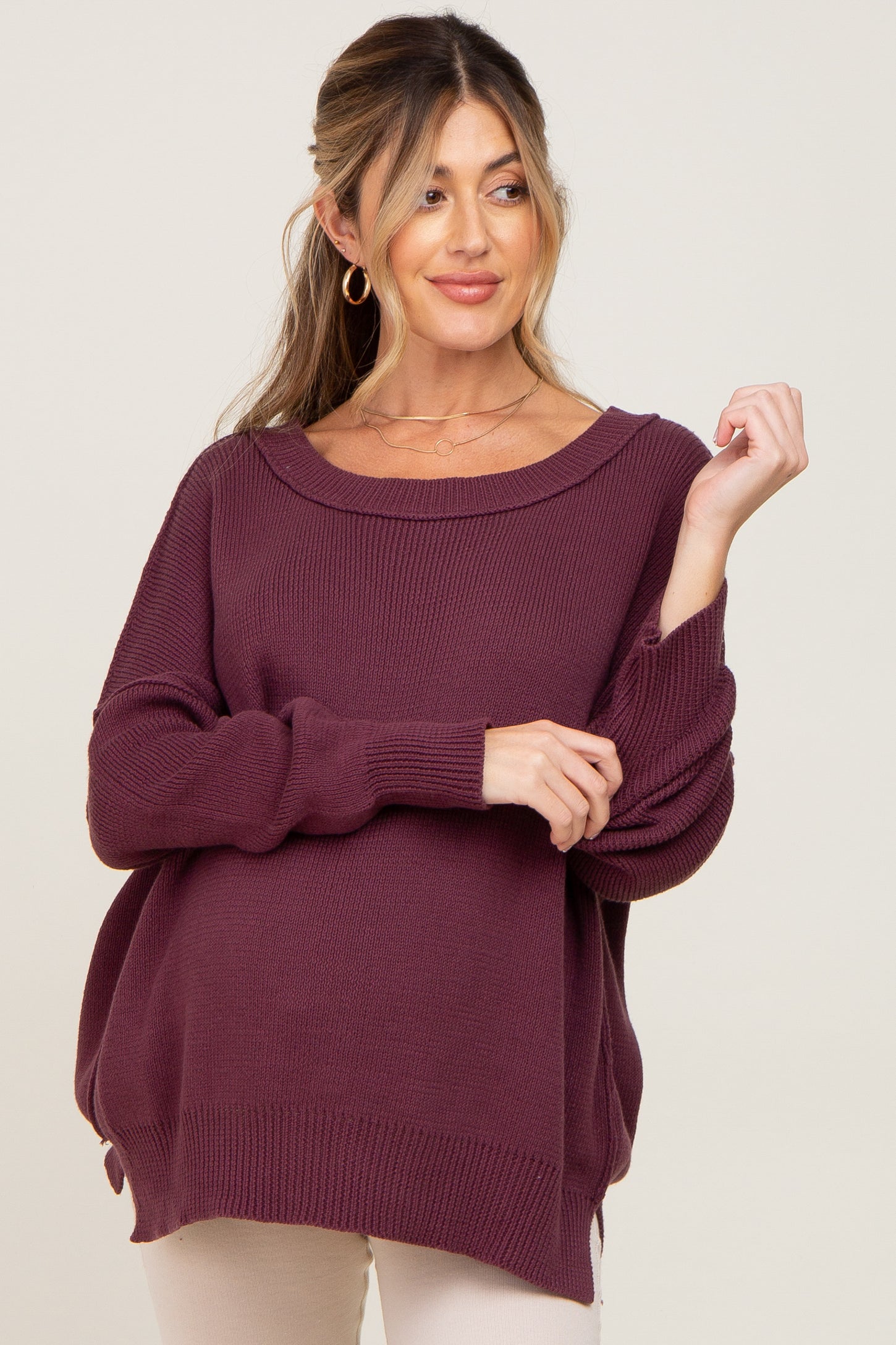 woman wearing a deep burgundy maternity sweater with a loose fit and rolled cuffs, showing a visible baby bump