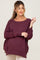 woman wearing a deep burgundy maternity sweater with a loose fit and rolled cuffs, showing a visible baby bump