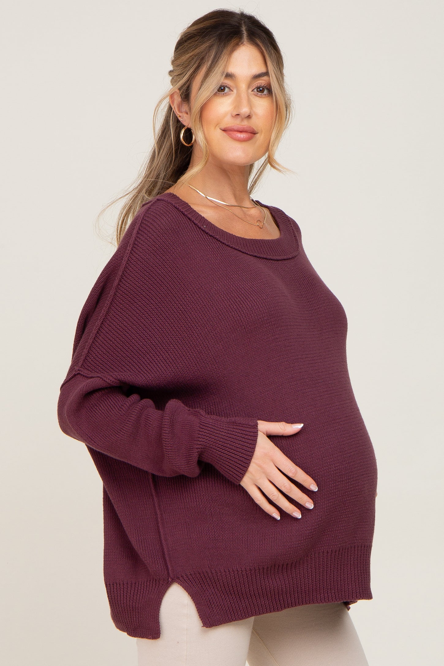 woman wearing a maroon maternity sweater with a relaxed fit and side slits, showcasing her baby bump