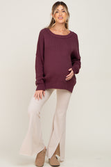 woman wearing a burgundy oversized maternity sweater and cream flared maternity pants, holding her baby bump