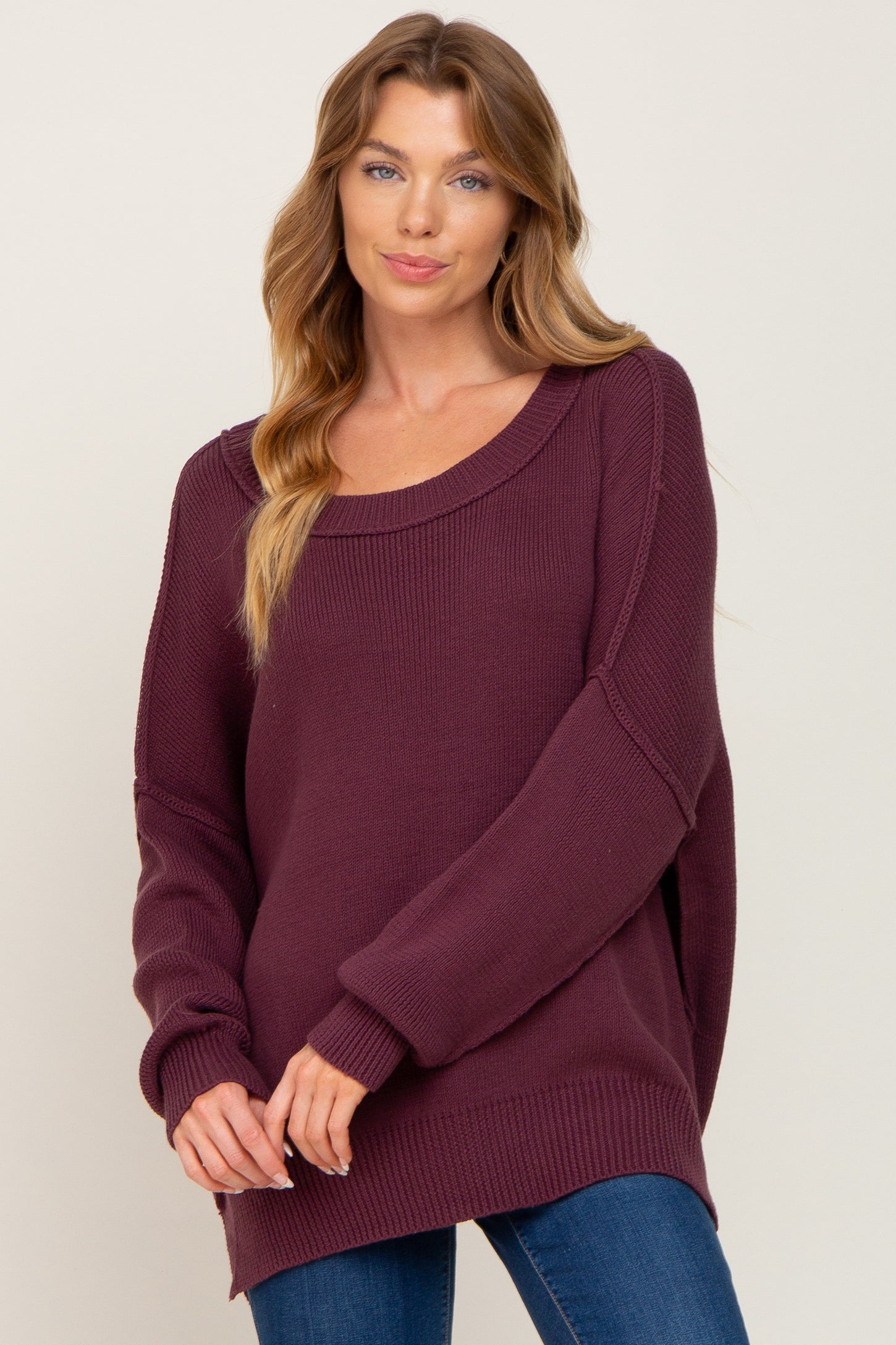 woman wearing a burgundy oversized sweater with a scoop neckline and long sleeves, paired with blue jeans