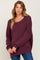 woman wearing a burgundy oversized sweater with a scoop neckline and long sleeves, paired with blue jeans
