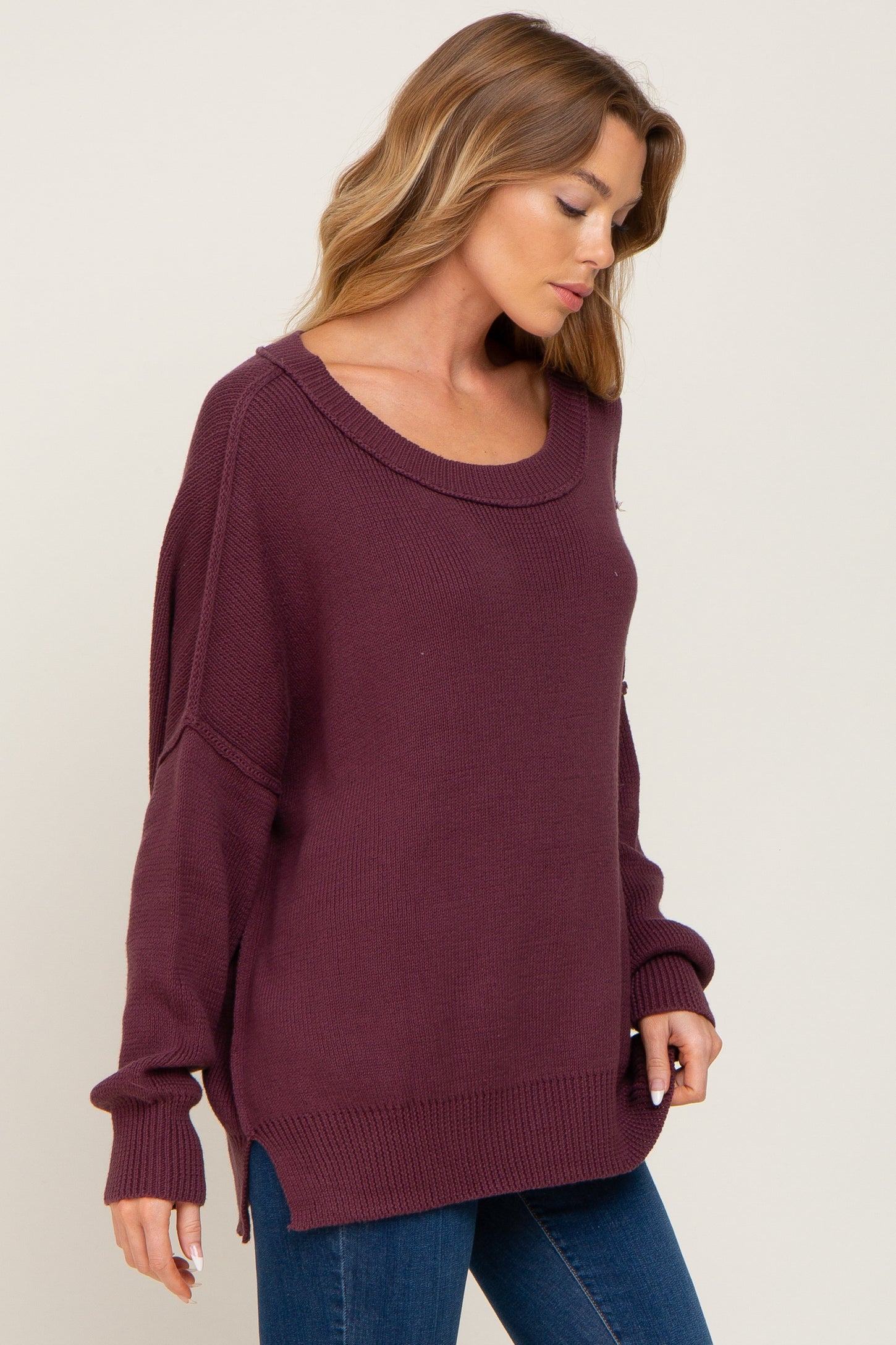 woman wearing a burgundy oversized sweater with a scoop neckline and side slits, paired with blue jeans