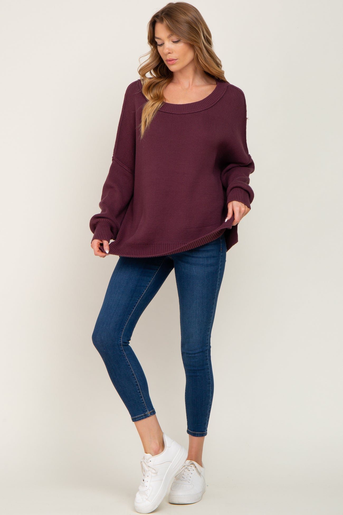 woman wearing a burgundy oversized sweater and blue skinny jeans with white sneakers