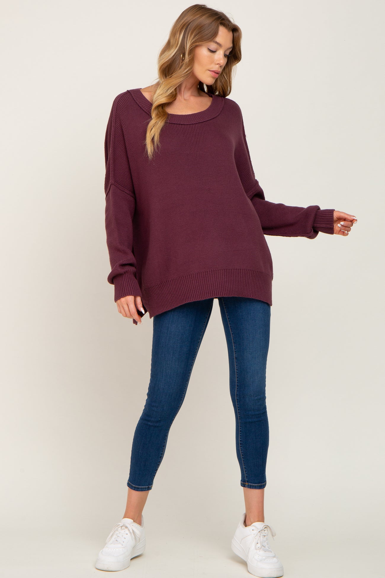 woman wearing a burgundy oversized sweater with a scoop neckline and skinny jeans, paired with white sneakers