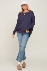 woman wearing a dark purple oversized knit sweater with blue flared jeans and a white baseball cap