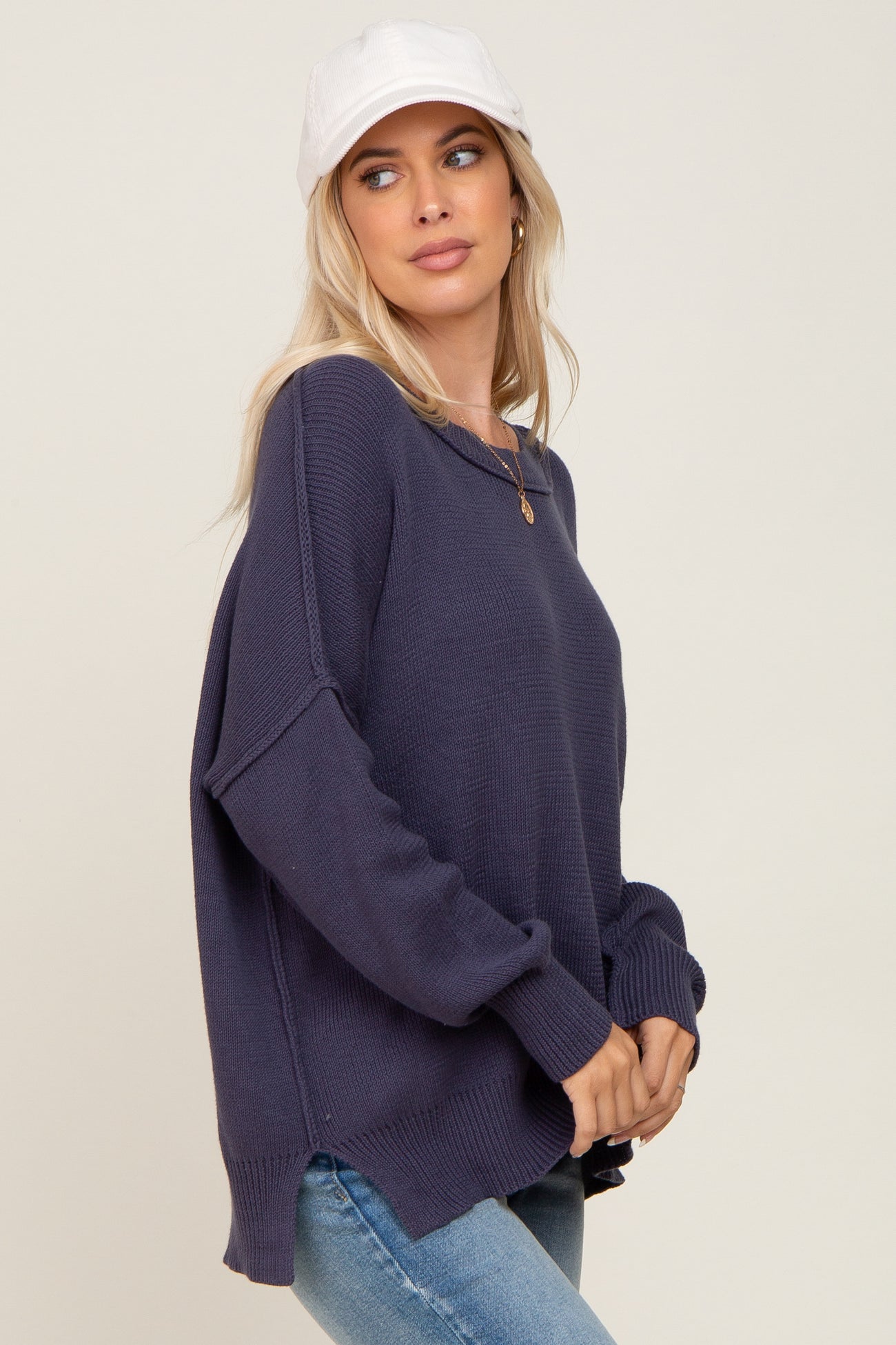 woman wearing a navy blue knitted sweater with side slits and relaxed fit, paired with light blue jeans and a white cap