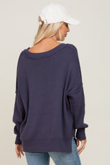 woman wearing a navy oversized sweater with a wide neckline, styled with a white baseball cap, seen from the back